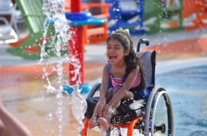 A child using a wheelchair enjoys a water sprinkler
